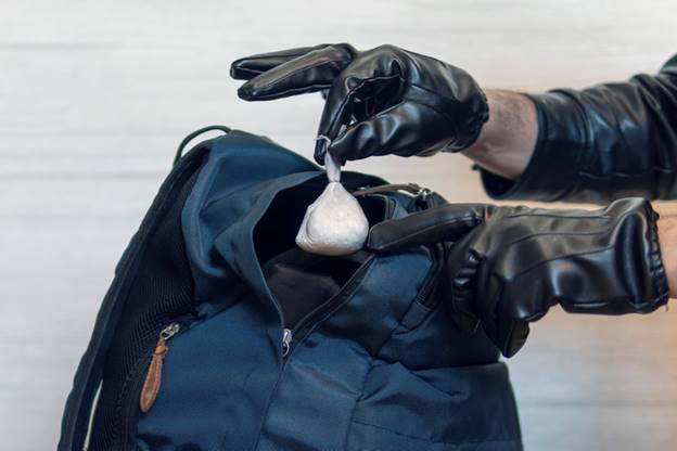 Here's a description of the image: A person wearing black leather gloves places a bag of white powder into a dark blue backpack. The photo illustrates evidence being suppressed or hidden.